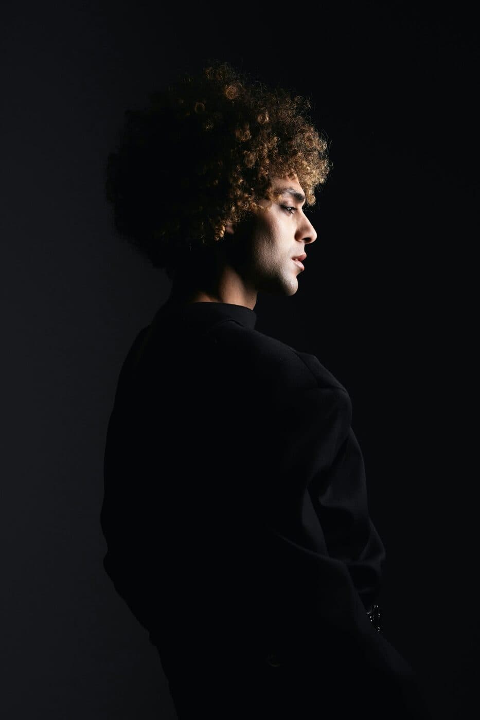 Side profile of a person with curly hair in dramatic studio light.